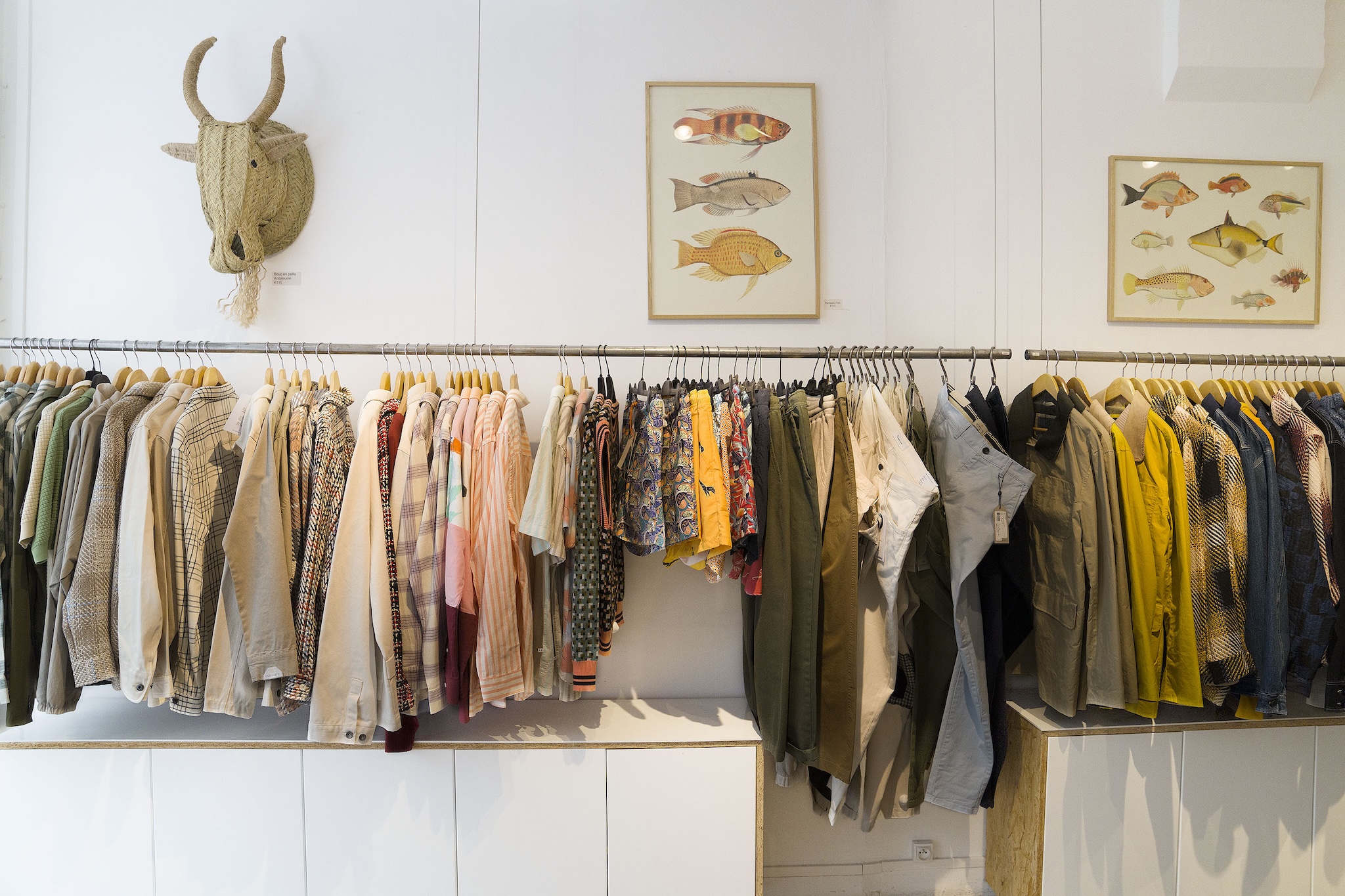 a long rack of clothing on hangers in a retail store. The space is white and has whimsical art.