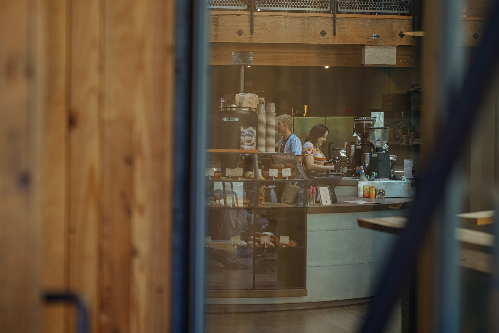 seen through a window, two baristas are making drinks