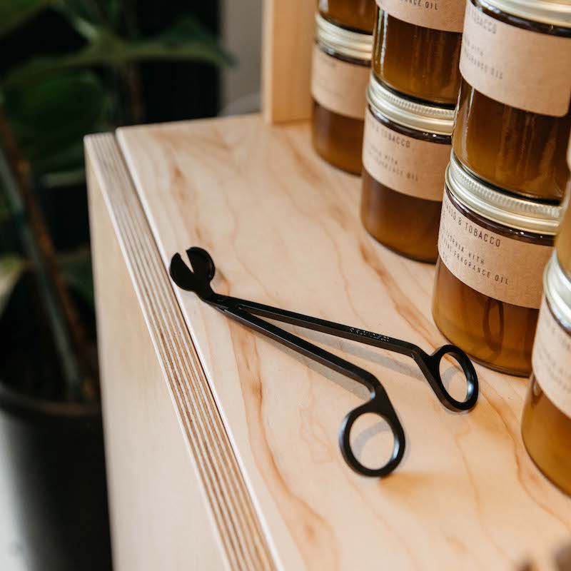 Black candle wick trimmer on wooden table.