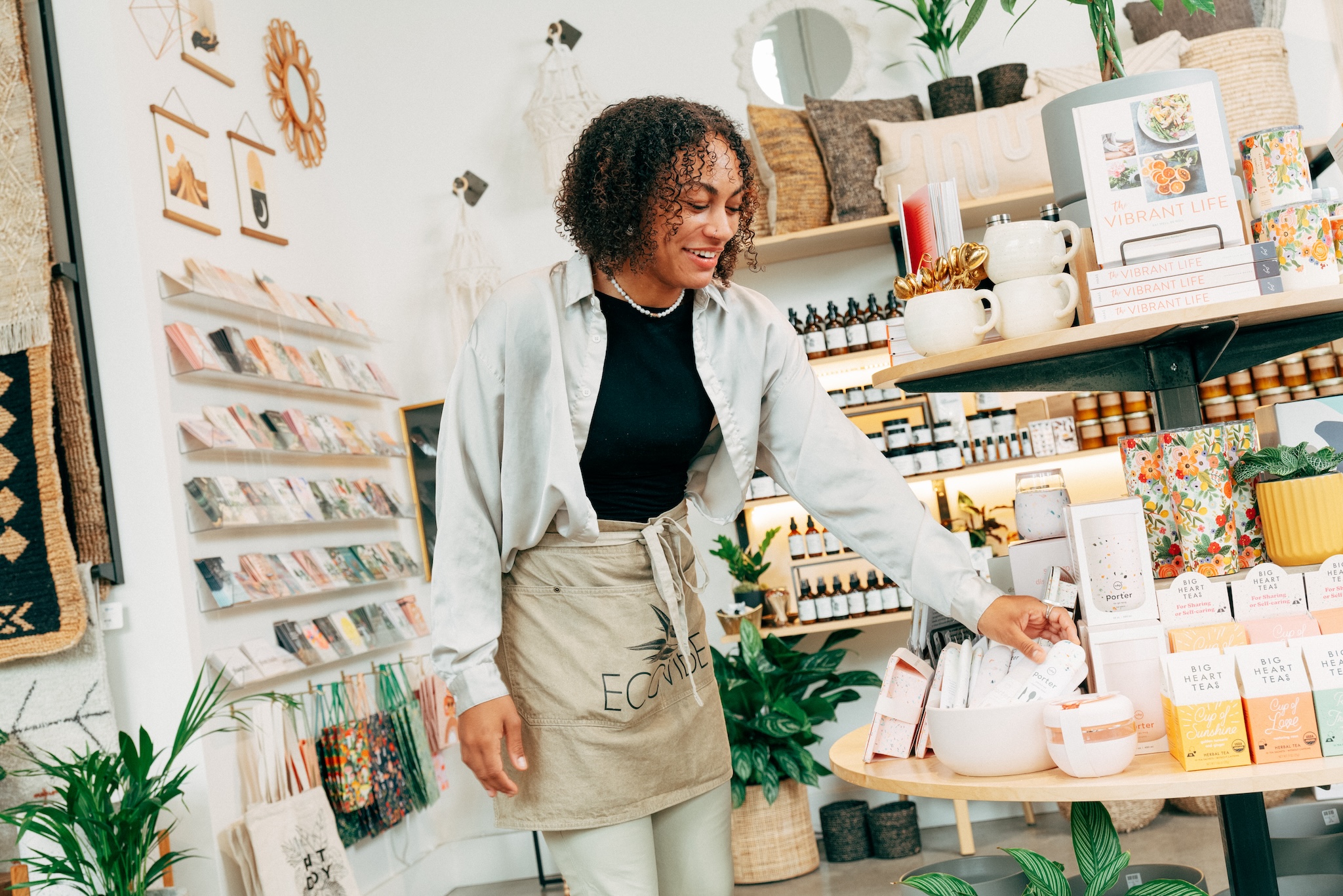 A shopkeeper straightens items on a display table inside a cute independent store