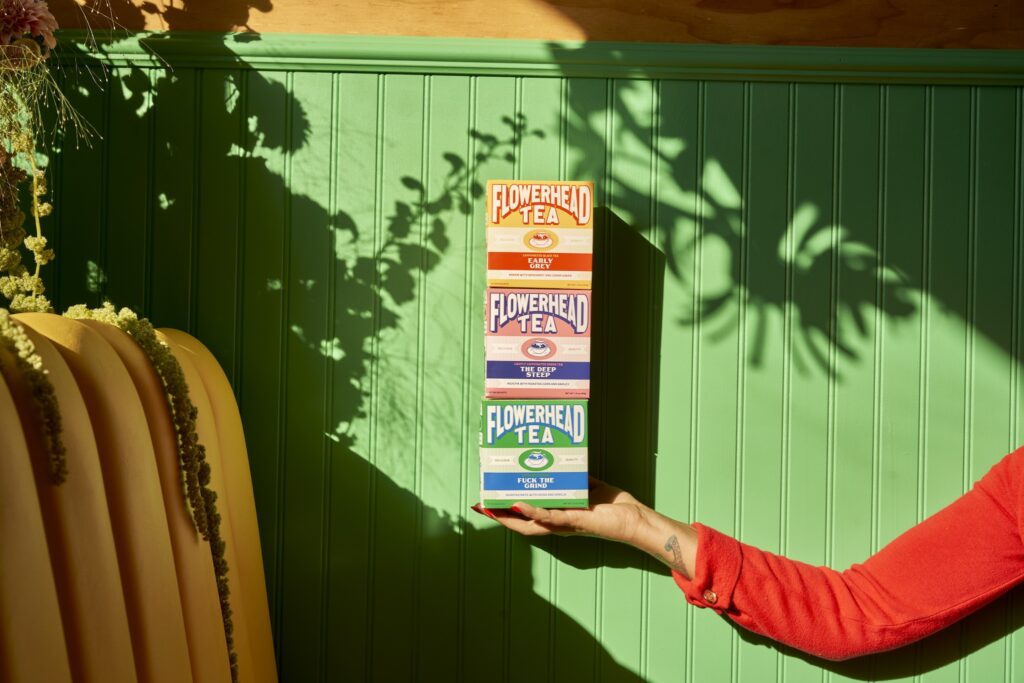 Person holding three Flowerhead tea boxes in front of green background.