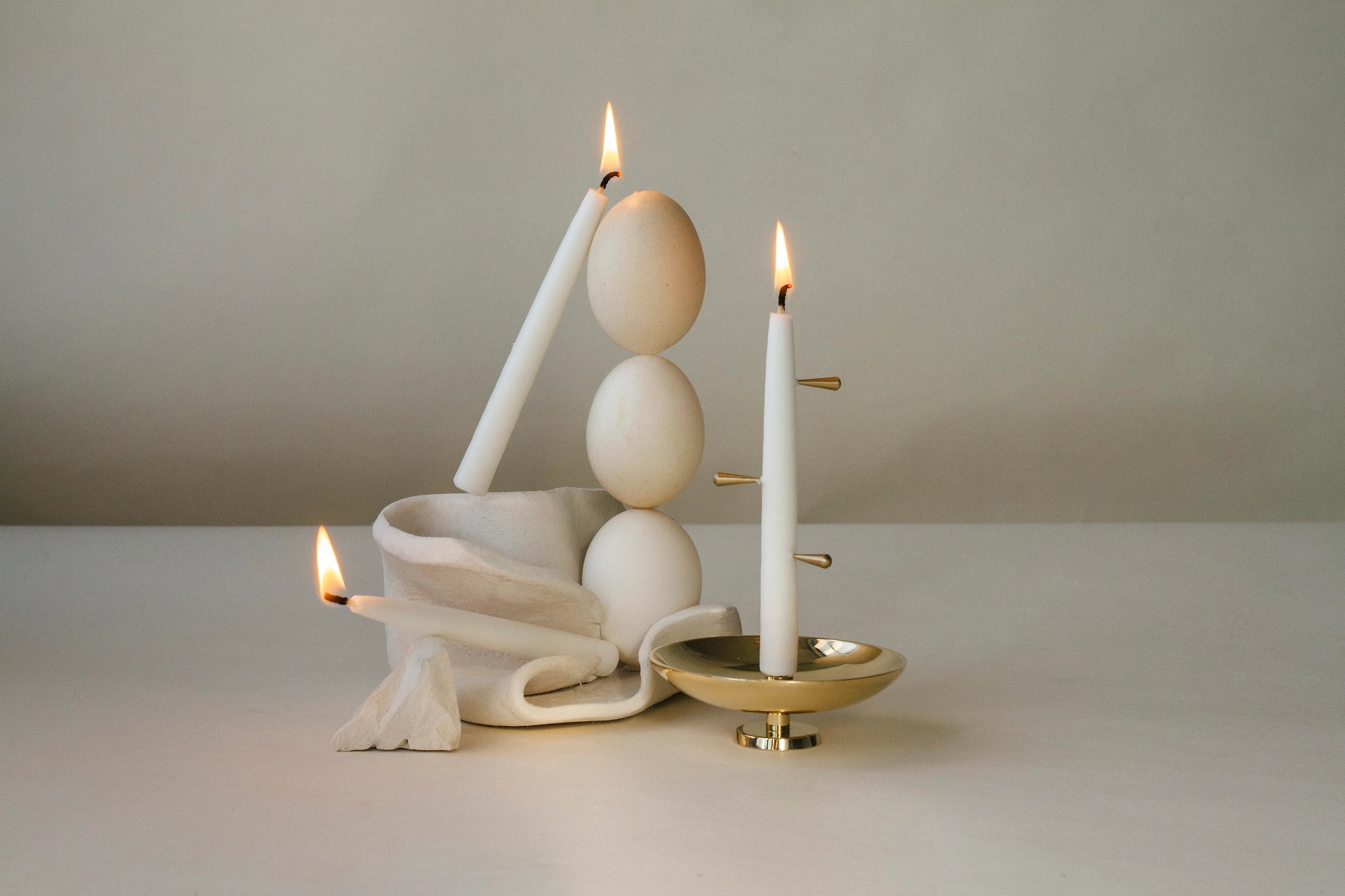 three taper candles are burning on minimalist wooden sculpture