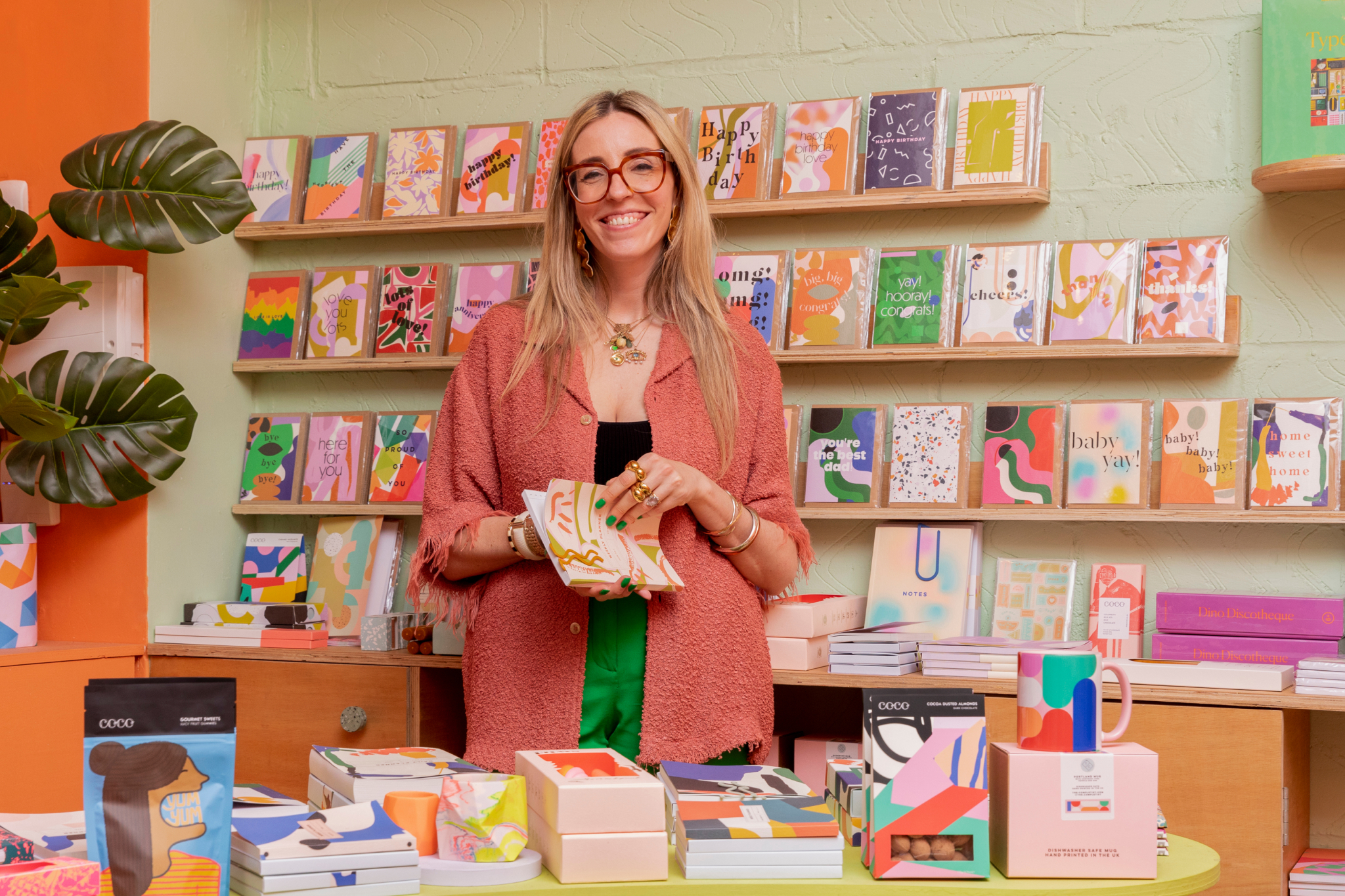 smiling shopkeeper stands in front of a table with colorful cards and books