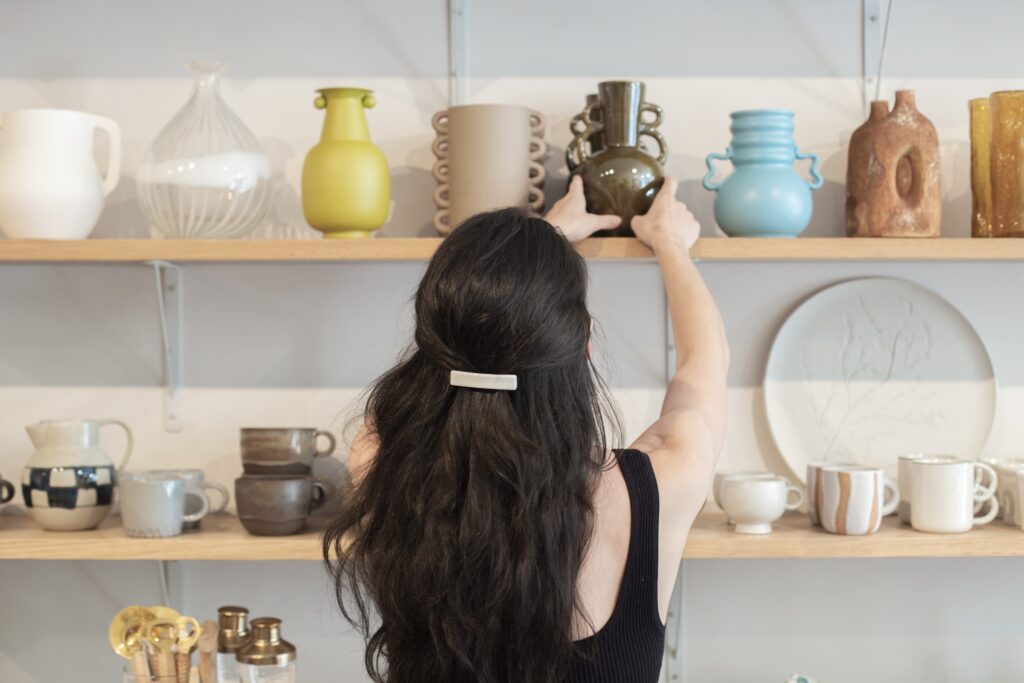 Commerçante arrangeant des étagères de vases et de vaisselle en préparation de l'ouverture de son magasin de décoration